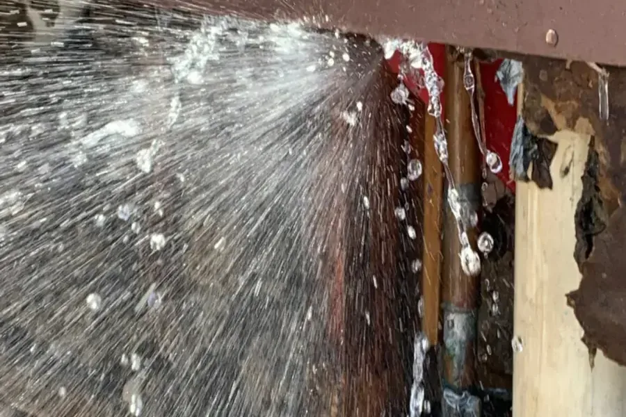 Water spraying out of a split pipe inside an opened wall cavity