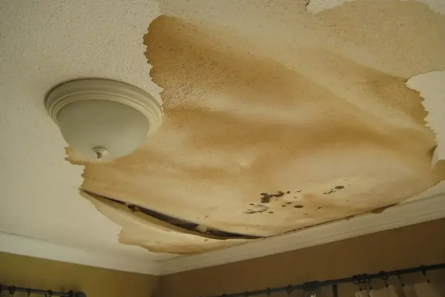 Stained ceiling drywall sagging around a light fixture below a leak