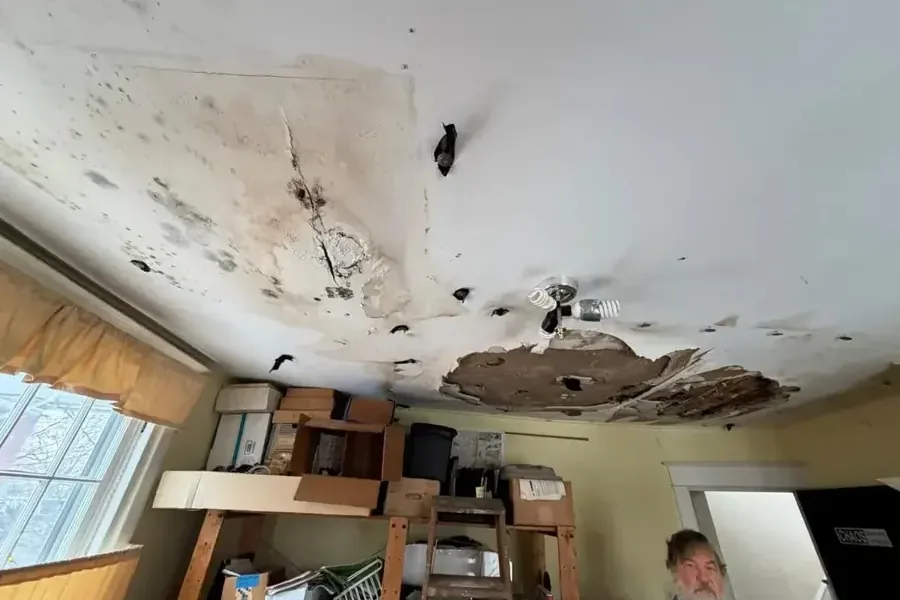 Bedroom ceiling torn open under a roof leak with soaked insulation hanging