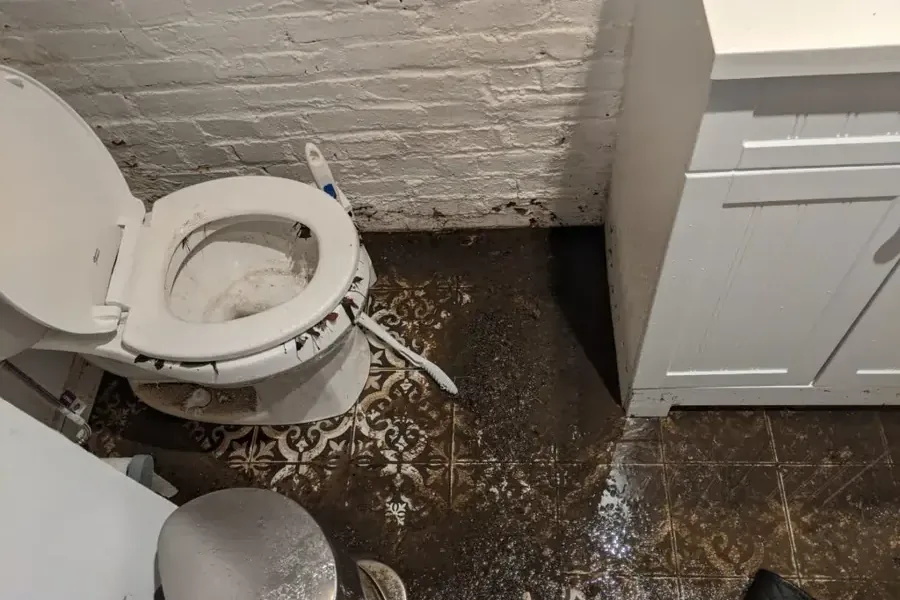 Dark sewage water from a toilet overflow spread over a bathroom floor