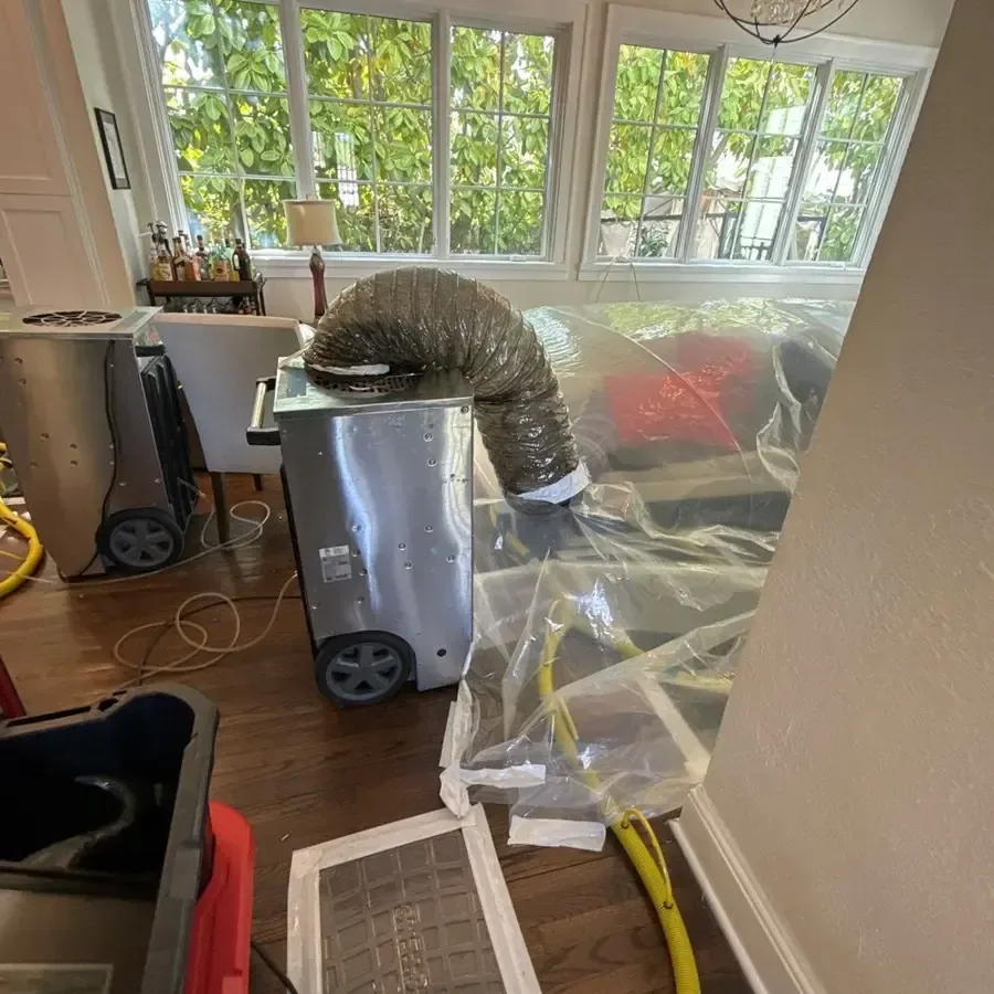 Dehumidifier ducted under plastic containment to dry a room with hardwood floors